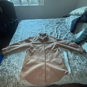 Beige overshirt från Vero Moda - Säljer en beige overshirt från Vero Moda i storlek L. Jackan har klassisk skjortkrage, långa ärmar och knappar framtill. Materialet är mjukt och känns som ullmix, perfekt för lager-på-lager. Enkel och clean design som funkar till många stilar.