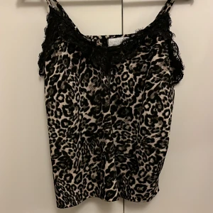 Leopardmönstrad linnetopp med spets - Säljer en snygg leopardmönstrad linnetopp från Samsa Collection. Toppen har tunna axelband och är dekorerad med svart spets längs urringningen. Materialet är glansigt och känns lyxigt.