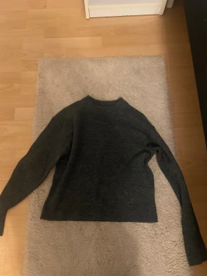 Mörkgrå stickad tröja med rund hals - Mysig mörkgrå stickad tröja med rund hals och långa ärmar. Tröjan har en enkel och clean design med ribbade muddar vid hals, ärmslut och nederkant. Perfekt för dig som gillar basic och stilrent.