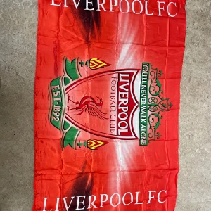 Liverpool FC halsduk i rött polyester - Stor och mjuk halsduk i rött med Liverpool FC:s klassiska klubbmärke och texten 'You'll Never Walk Alone'. Halsduken har gröna och gula detaljer samt vita bokstäver. Perfekt för att visa ditt stöd på matchen eller hemma.