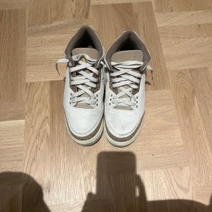 Nike Air Jordan 3 sneakers beige - Nike Air Jordan 3 sneakers i beige och bruna toner med klassisk snörning och rund tå. Skorna har detaljer i mocka och skinn samt det ikoniska Jordan-loggan i guld på hälen. Snyggt mönstrad panel runt sulan och vadderad plös för extra komfort.