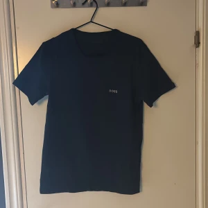 Svart t-shirt från BOSS, storlek M - Svart t-shirt från BOSS i storlek M. Klassisk design med rund hals och korta ärmar. Diskret BOSS-logga på bröstet. Tillverkad i mjuk bomull som känns skön mot huden. Perfekt för dig som gillar stilrena och enkla plagg med premiumkänsla.