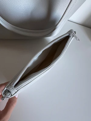 Ljusgrå shoppingväska med innerficka - Stilren ljusgrå shoppingväska i syntetmaterial med lätt struktur och dubbla handtag. Väskan har en rymlig insida med ljusrosa foder och en avtagbar innerficka med dragkedja, perfekt för småprylar. Enkel och modern design som passar till det mesta. Bundle är aktiverat🩶