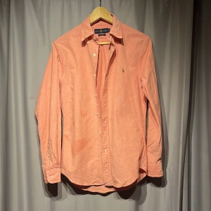 Slim fit rosa skjorta från Ralph Lauren - Fräsch rosa skjorta från Ralph Lauren i slim fit stretch oxford. Klassisk krage, långa ärmar och knappar framtill. Ikonisk broderad logga på bröstet. Nypris 1500kr