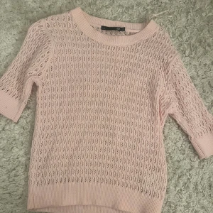 Ljusrosa stickad tröja från 157 - Säljer en ljusrosa stickad tröja från 157 i storlek XS. Tröjan har ett snyggt hålmönster och ribbade muddar vid hals, ärmslut och nederkant. Modellen har korta ärmar och är perfekt för vår och sommar. Superfin att styla med jeans eller kjol!