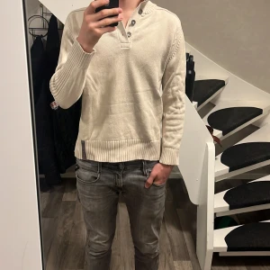  Beige stickad sweater  -  Beige stickan, sweater med en grå detalj längst ner och fyra knappar vid halsen. Väldigt skön och passar folk som är mellan 170-180