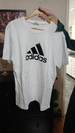 Vit Adidas t-shirt med logga - Snygg vit t-shirt från Adidas med stor svart logga på bröstet. Klassisk rund hals och korta ärmar, perfekt för dig som gillar sportig och enkel stil. Köpt från Turkiet aldrig använt. Strycker innan jag skickar de:) klicka järna på bilden.