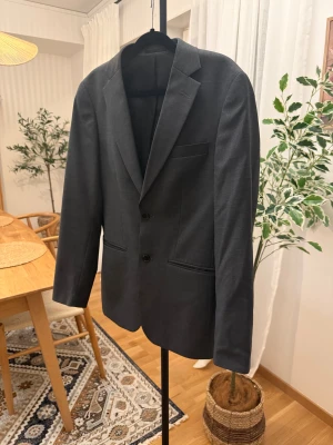 Mörkgrå kostym från Dressmann slim fit - Säljer en stilren mörkgrå kostym från Dressmann i slim fit-modell. Kavajen har två knappar, klassiska fickor och snyggt snitt. Byxorna har bälteshällor och enkel knappstängning. Materialmix av ull och polyester med lite stretch för extra komfort. Kavajens storlek: 44, dvs S. Byxans storlek: 32/32