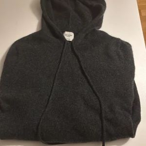 Mörkgrå hoodie i kashmir från John Henric - Mjuk och lyxig mörkgrå hoodie från John Henric i 100% kashmir. Tröjan har huva med snörning och långärmad design, perfekt för dig som gillar stilren och bekväm look. Passar dig som vill ha något extra skönt och snyggt i garderoben.