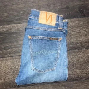 Nudie Jeans High Kai - Snygga blå jeans från Nudie Jeans, modellen High Kai med midwaist. Jeansen har slim passform och klassisk femficksdesign med orangea sömmar och Nudie-logga på bakfickan. Tillverkade i mjukt bomullsmaterial med lätt tvättad look.