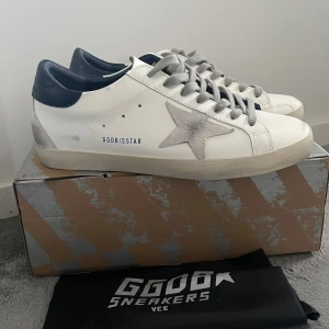 Golden Goose - Golden Goose sneakers i vitt skinn med grå mockadetaljer, grå snörning och mörkblå häl. Nya och helt oanvända. Kommer med originalkartong och dustbag.