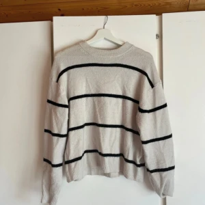 Vit och svart randig stickad tröja - Mysig stickad tröja i vit färg med svarta horisontella ränder. Tröjan har rund hals och långa ärmar med ribbade muddar. Perfekt för dig som gillar enkel men snygg stil och vill ha något som är både bekvämt och trendigt.