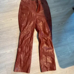 Vinröda skinnbyxor från Gina Tricot - Snygga röda skinnbyxor från Gina Tricot i rak modell. Byxorna har midjehöga hällor för bälte och klassisk dragkedja framtill. Materialet är syntetiskt skinn med en mjuk insida, perfekt för dig som vill ha en cool look.