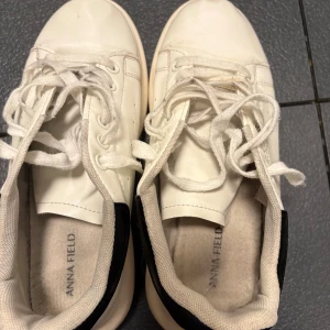 Vita sneakers från Anna Field - Snygga vita sneakers från Anna Field med svart detalj på hälen. Skorna har rund tå, platt sula och klassisk snörning. Perfekt för dig som gillar stilrena och enkla sneakers. Jag köpte dessa för att ha på studenten, gick in dem för att inte ha skav och användes under studenten. Sen har de tyvärr inte kommit till användning mer, därav säljer jag dem. De är i mycket fint skick även fast de är använda. Allt ska bort så accepterar alla rimliga bud🌸🙌🏼