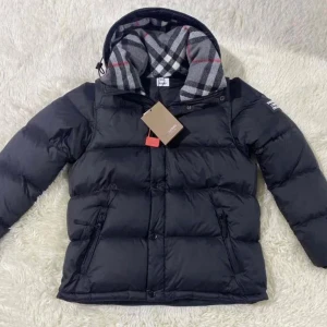 Svart pufferjacka från Burberry - Svart pufferjacka från Burberry med klassisk rutig huva i grått, vitt och rött. Jackan har dragkedja och knappar med Burberry-logga, två sidofickor med dragkedja och quiltad design. Perfekt för kalla dagar med sin tjocka och fluffiga känsla.