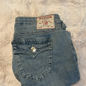 True Religion ljusblå bootcut jeans - Säljer ett par ljusblå jeans från True Religion med bootcut passform. Jeansen har snygga silverfärgade knappar och ikoniska broderade bakfickor med lock. Klassisk jeanslook i mjukt bomullsmaterial och med normal passning. Perfekt för dig som gillar detaljer och streetstil. Säljer på grund av dålig användning och för stor storlek. För intresse kontakta och fråga om mer om det är något! Säljs nu för 1300kr säljer nu för 1000kr och är i bra skick.