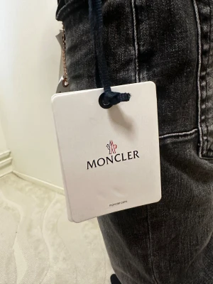 Vit vindjacka från Moncler med huva - Snygg vit vindjacka från Moncler med huva och dragkedja framtill. Jackan har Moncler-logga på ärmen och coola rödblå detaljer på huvan. Långärmad och med snörning vid halsen. Perfekt för dig som gillar stilrena och sportiga plagg.