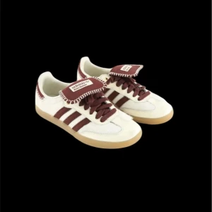 Adidas Samba Wales Bonner vit/brun - Adidas Samba Wales Bonner sneakers i vitt och mörkbrunt med klassiska tre ränder på sidan. Skorna har en unik broderad kant på plösen och hälpartiet, samt snörning och platt gummisula. Ovandelen är i skinn med detaljer i mocka och päls för extra textur.