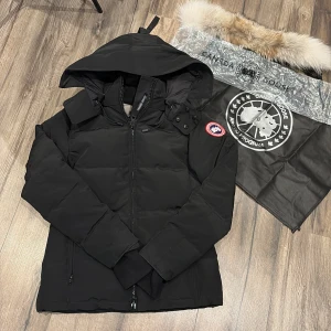 Svart Canada Goose Chelse Parka M - Säljer en svart Canada Goose Chelse Parka i storlek M för TJEJ som även går späna runt midjan. Jackan har huva, dragkedja och ikonisk röd-vit-blå patch på ärmen. Vadderad design med dunfyllning och praktiska fickor. Perfekt för kalla vinterdagar och har snygg, stilren look. helt ny aldrig andvänd passar s även 