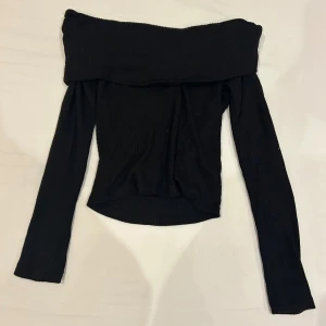 Svart offshoulder topp från Gina Tricot - Svart ribbad offshoulder topp från Gina Tricot i storlek S. Toppen har lång ärm och en bred kant upptill som ger en snygg offshoulder-look. Materialet är mjukt och stretchigt. 
