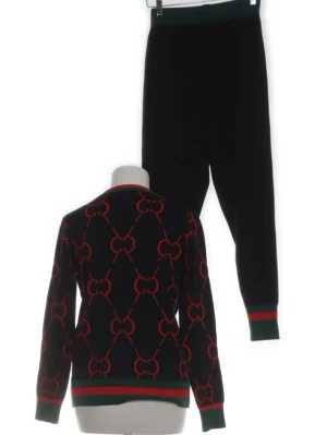 Svart loungewear-set med rött mönster - Snyggt svart loungewear-set med matchande tröja och byxor. Tröjan har ett rött kedjemönster och gröna samt röda ribbade muddar vid ärmslut, hals och midja. Byxorna har samma gröna och röda detaljer vid benslut och midja. Perfekt för chill dagar hemma.