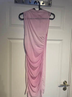 Rosa omlottklänning från Zara - Säljer en snygg rosa omlottklänning från Zara i storlek XS. Klänningen har draperade detaljer längs sidorna och är ärmlös med en tight passform. 