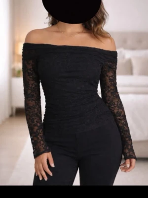 Svart offshoulder spets topp - Trendig svart offshoulder topp med långa ärmar i genombruten spets. Sitter tight och har en elegant, feminin look som passar perfekt till både jeans och kjol. Toppens material är stretchigt och följsamt. Endast använd 1 gång 