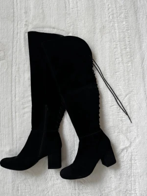 Svarta overknee stövlar med snörning - Säljer ett par nya svarta overknee stövlar i mockaimitation med chunky klack och snörning längs baksidan, vilket gör dem justerbara i bredden. Stövlarna har dragkedja på insidan. 
