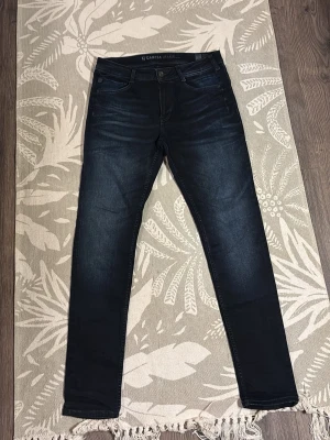 Mörkblå slim fit jeans Garcia - Snygga mörkblå slim fit jeans från Garcia Jeans med klassisk femficksmodell och subtila slitningar. Jeansen har normal midja och smala ben, perfekta till en avslappnad men ändå stilren look. Materialet är mjukt denim med stretch för extra komfort.