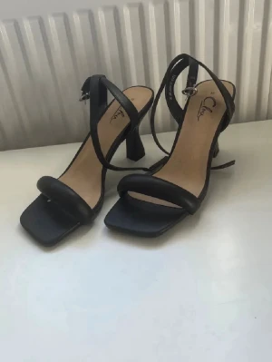 Svarta klackskor stl 36 - Stilrena svarta pumps från Clou med fyrkantig tå och smala remmar. Klackarna är ganska låga med en tjockare klack vilket ger lite mer stabilitet. Helt oanvända, endast testade hemma då de var för små när dom kom och jag har inte skickat tillbaka dom. Storlek 36.