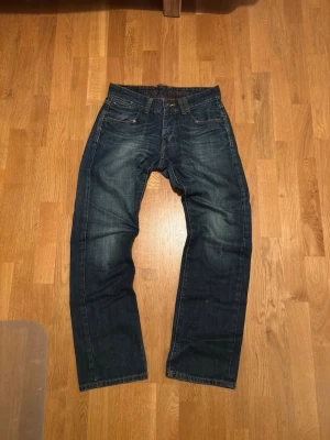 Vintage Low Waist Tommy Hilfiger Jeans - Vintage Tommy Hilfiger jeans i mörkblå tvätt med raka ben och fem fickor. Jeansen har en tidlös look med knappgylf och är tillverkade i slitstark bomullsdenim. Perfekta för dig som gillar en enkel och clean stil.                                              Midjemått: 40cm Längd: 103cm Fotvidd: 21cm