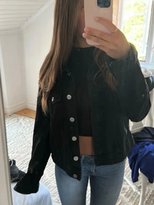 Svart jeansjacka med silverknappar - Snygg svart jeansjacka med klassisk passform och silverfärgade knappar framtill. Jackan har två bröstfickor med lock och knappar, samt en rak och tidlös design som passar till det mesta.