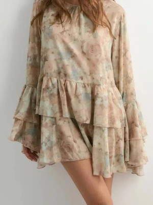 Blommig volangklänning i pastell - Supersöt kortklänning med blommigt mönster i beige, ljusblått och rosa toner. Klänningen har långa, vida ärmar med volangdetaljer och volanger även i nederkant. Perfekt för sommarens alla tillfällen!
