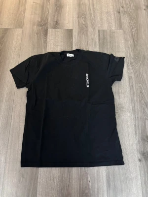 Svart t-shirt med logga - Snygg svart t-shirt med diskret logga tryckt vertikalt på bröstet. Klassisk rund halsringning och korta ärmar. Perfekt för en clean och stilren look.