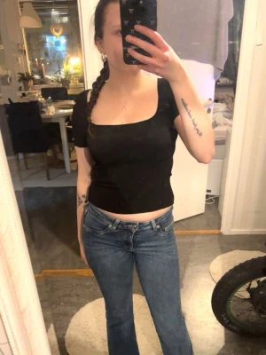 Svart croppad topp med fyrkantig ringning - Trendig svart croppad topp med fyrkantig ringning och korta ärmar. Sitter tajt och har en stilren, minimalistisk look som passar perfekt till jeans eller kjol. Materialet ser ut att vara stretchigt och bekvämt.