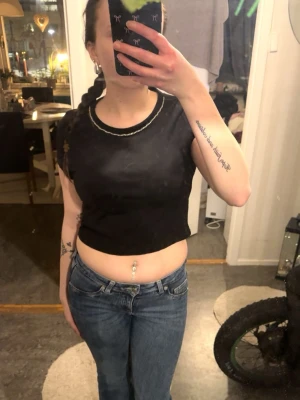 Svart croppad topp med kort ärm - Snygg svart croppad topp med korta ärmar och rund halsringning. Perfekt för att skapa en trendig look till jeans eller kjol. Enkel och stilren design som passar till många outfits.