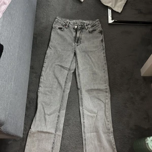 Grå mid wide jeans med raka ben - Säljer ett par grå jeans med mid wide fit och raka ben. Jeansen har normalhög midja, fem fickor och bälteshällor. Storlek 24 i midjan och längd 32. Klassisk knapp och dragkedja framtill. Perfekta för en avslappnad och trendig look.