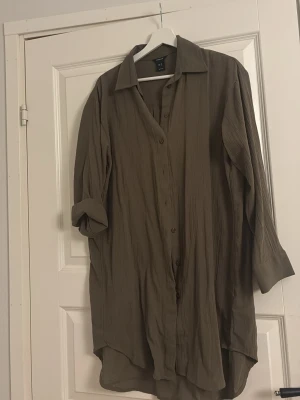 Grön längre  skjorta från Lindex - Lång skjorta i grön nyans från Lindex. Skjortan har knappar framtill, klassisk krage och långa ärmar med manschett. 