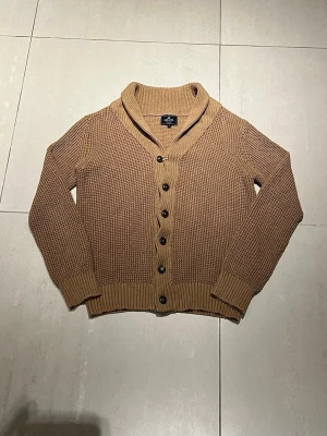 Beige kofta från Park Lane - Säljer en beige stickad kofta från Park Lane med grov struktur, sjalkrage och svarta knappar framtill. Koftan har långa ärmar och ribbade muddar vid ärmslut och nederkant. Perfekt för lager-på-lager och chill stil.