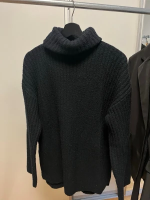 Svart stickad polotröja från BikBok - Mysig svart stickad polotröja från BikBok med ribbad struktur. Tröjan har lång ärm och en hög, bred polokrage som ger en avslappnad och trendig look. Perfekt för kalla dagar och enkel att matcha med olika outfits.