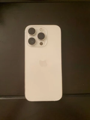 Vit iPhone med trippelkamera 1TB - Snygg vit iPhone 14 pro med stilren design och rundade hörn. Baksidan är i glas och mobilen har tre stora kameralinser i hörnet för grymma bilder. Apple-loggan syns tydligt på baksidan. Perfekt för dig som vill ha en modern och kraftfull smartphone.