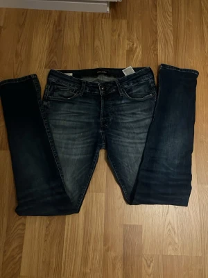 Mörkblå slim fit jeans från Jack & Jones - Snygga mörkblå slim fit jeans från Jack & Jones med slitningar och tvättade detaljer på framsidan. Klassisk femficksmodell med dragkedja och knapp i midjan. Perfekta för en avslappnad och trendig look.