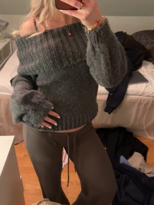 Mörkgrå off shoulder stickad tröja - Mysig mörkgrå stickad tröja med bred ribbad off shoulder-krage och långa ärmar. Tröjan har en avslappnad passform. Materialet är mjukt och fluffigt, vilket gör den extra skön att bära.
