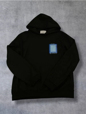 Casablanca Hoodie - Svart hoodie från Casablanca med tryck i blått och beige på bröstet och ryggen. Stort grafiskt motiv på ryggen med texten 'Casa Blanca'. Klassisk passform med huva och ribbade muddar. Perfekt för en stilren och modern look.
