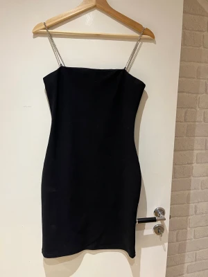 Figurnära miniklänning  - Snygg svart miniklänning i bodycon modell med smala band i silverfärgade diamanter. Endast använda en gång.