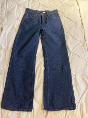 Mörkblåa vida jeans - Säljer ett par mörkblåa jeans med rak och vid passform. Klassisk femficksmodell med hög midja och knappgylf. Jeansen har en enkel design utan slitningar och är tillverkade i denim. Perfekta för en avslappnad och trendig look.