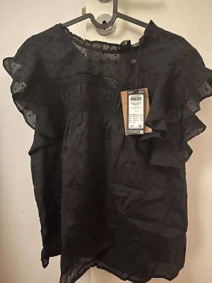 Svart volangblus med prickar -  svart blus med volangärmar och prickmönster. Lappen är kvar