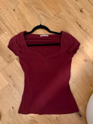 Vinröd ribbad topp från Anna Field - Snygg vinröd ribbad topp från Anna Field med korta ärmar och v-ringad hals. Figurnära passform och stretchigt material som sitter bekvämt. Perfekt att styla med jeans eller kjol för en trendig look.