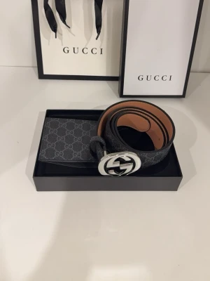 Svart Gucci bälte med GG-spänne - Snyggt svart bälte från Gucci med klassiskt GG-mönster och ett stort, silverfärgat GG-spänne. Bältet har en lyxig känsla med insida i brunt skinn och passar perfekt till jeans eller kostymbyxor.