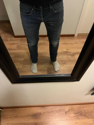 Dondup Jeans George skinny fit  - Säljer ett par mörkblå slim fit jeans från Dondup med lätt slitna detaljer på knäna och klassiska fem fickor. Jeansen har en snygg tvätt och sitter tajt längs benen. Perfekta för en trendig och avslappnad stil.